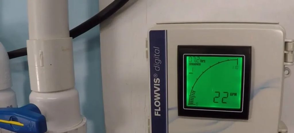 Flowvis digital flow meter display reading 22 GPM mounted next to pool PVC plumbing